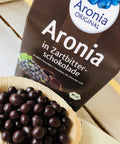 dried aronia berries covered with dark chocolate on wooden spoon